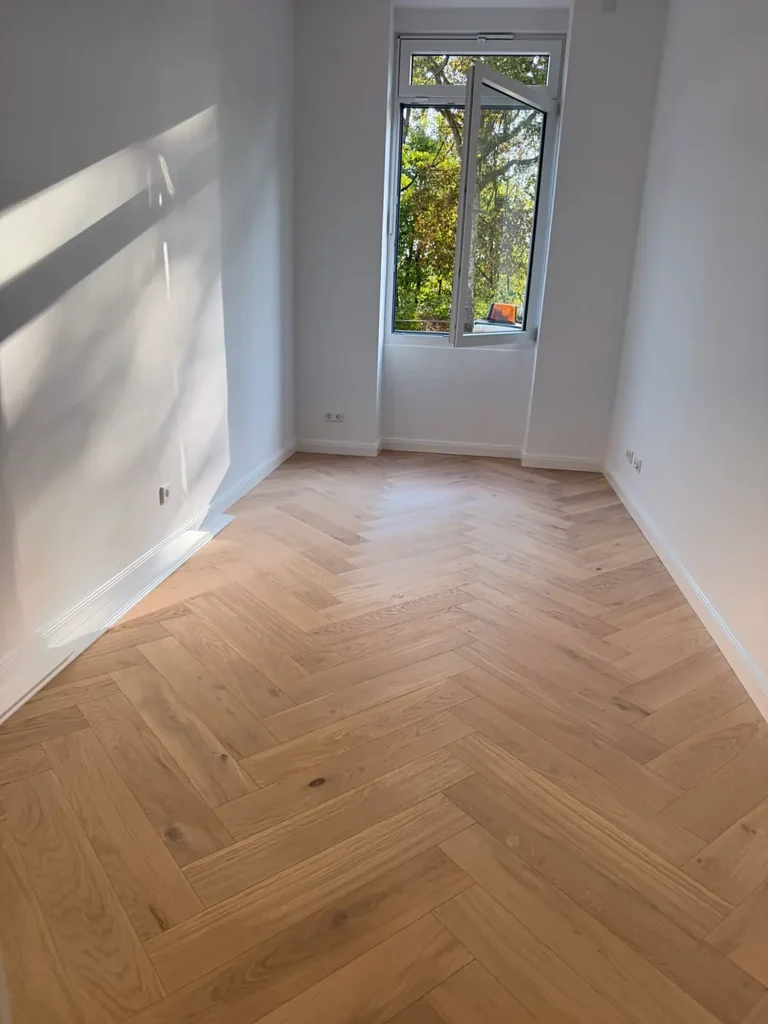 Zimmer mit Fischgrätparkett und Fenster ins Grüne