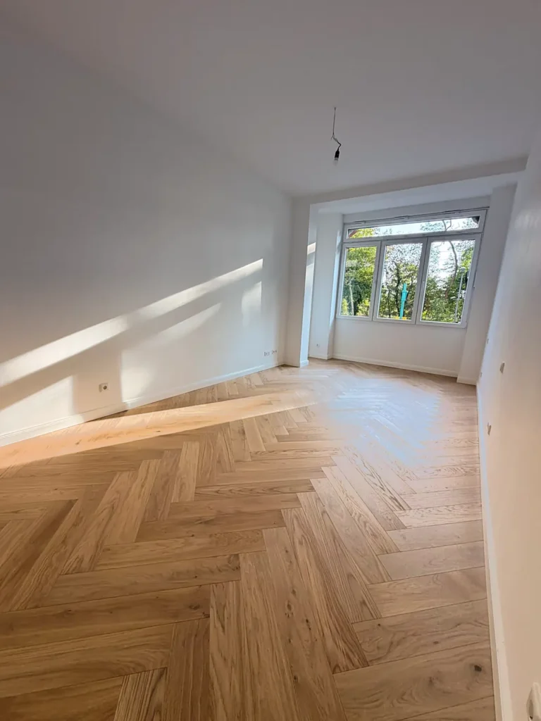 Sonniger Raum mit Fischgrätparkett und breitem Fenster